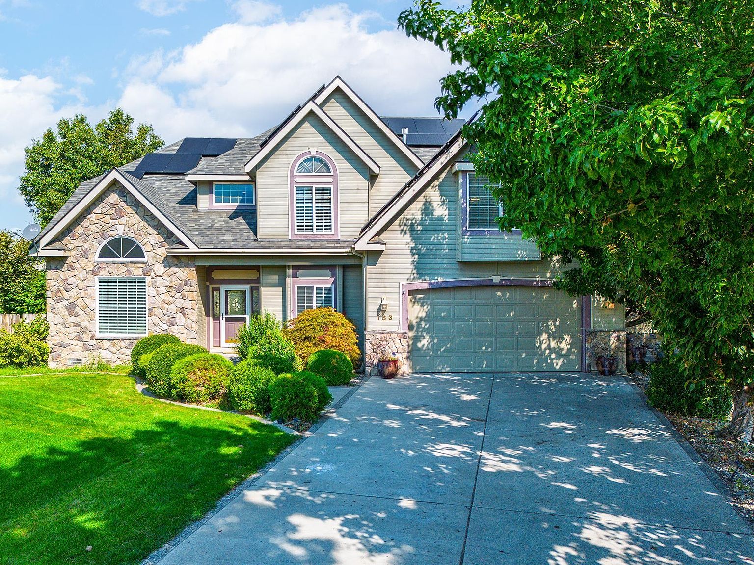 A landscaped suburban home beneath mature trees, with the roof and front approach in view.