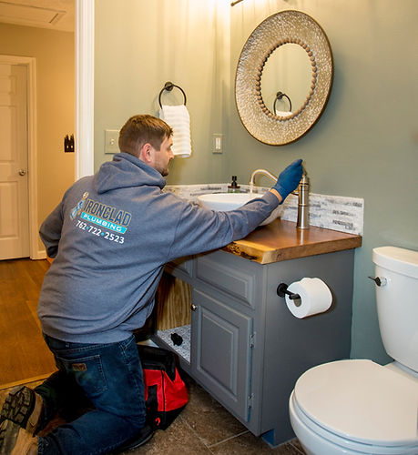 A plumber at work beside a bathroom sink and faucet.